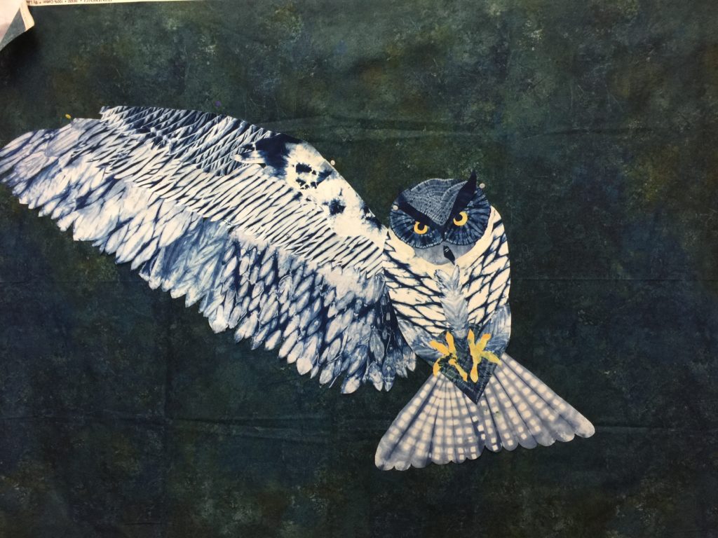 In progress art quilt with body of owl and one wing floating on background fabric