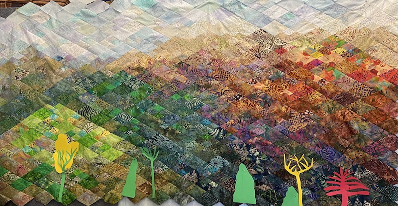 pieced quilt top depicting mountains in full color of seasons with pale sky