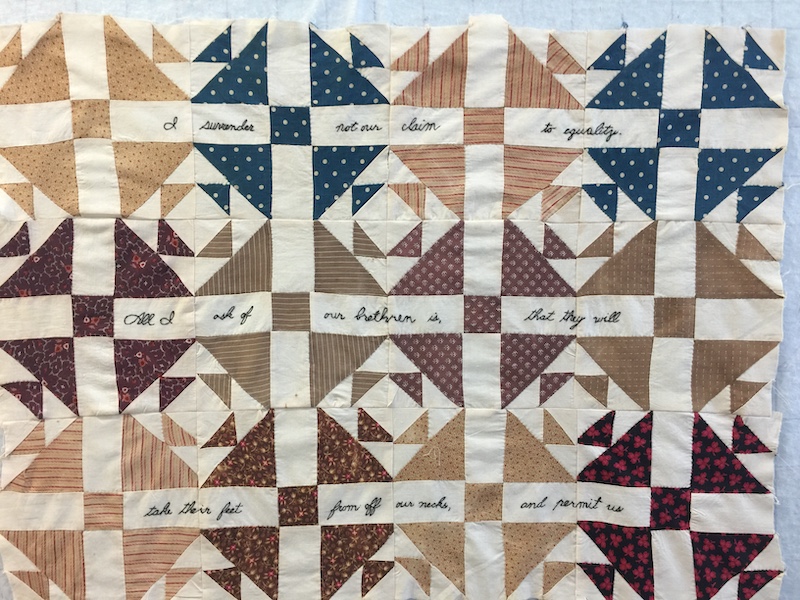Shoofly quilts blocks with words embroidered in black on the cream spaces. The words read, "I surrender not our claim to equality. All I ask of my brethren is that they will take their feet from off our necks and permit us..."