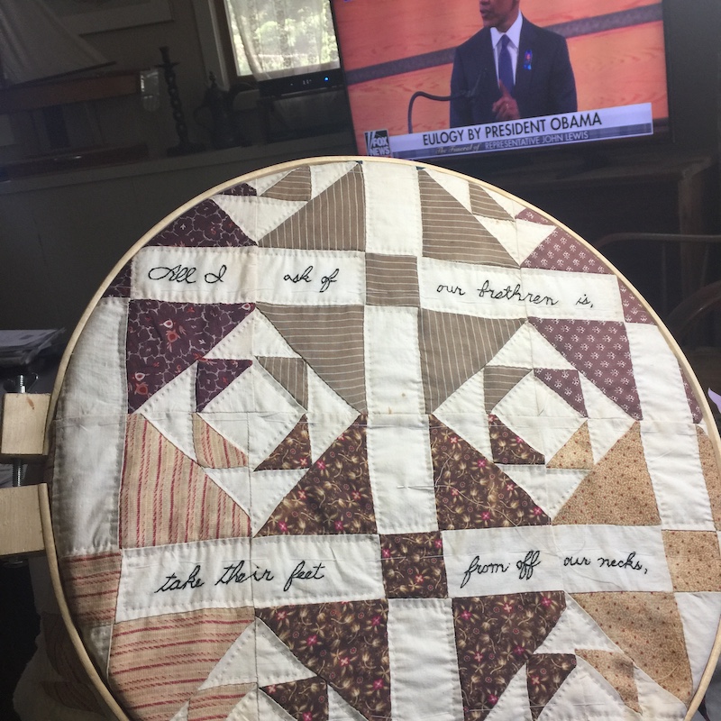 Antique quilt blocks in a wooden quilting hoop. The blocks are shoofly blocks and they have words hand embroidered on them.