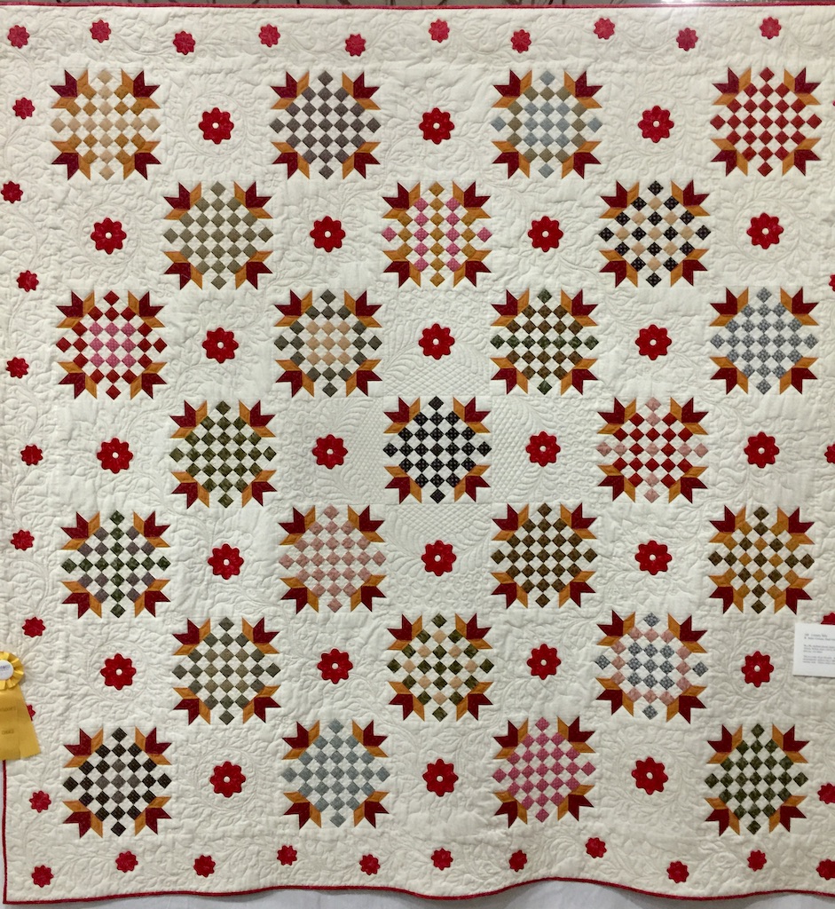 Country Mile quilt with cream background, checkerboard squares and appliquéd red flowers.