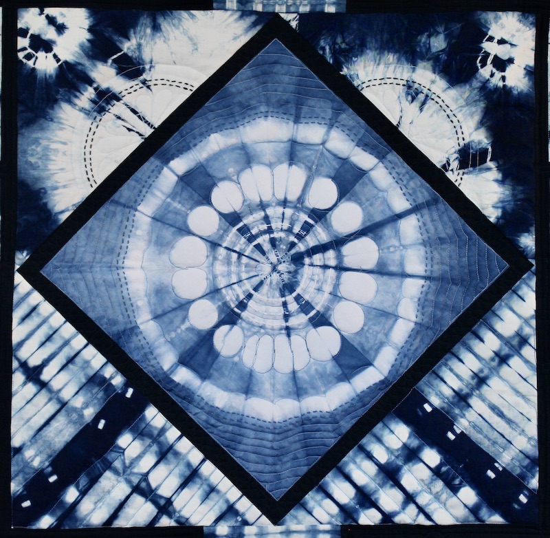 Shibori died indigo blue and white art quilt with sunburst circular image in center of on point square.