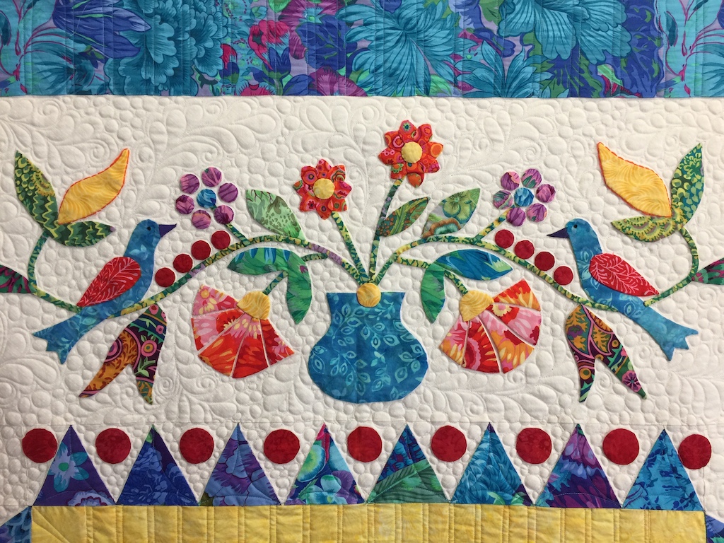 Applique quilt with white background and brightly colored floral and bird motifs.
