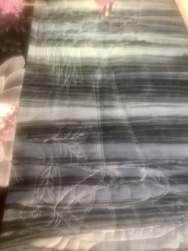 Gray and black fabric with chalk drawing of crane being stitched on a long arm quilting machine