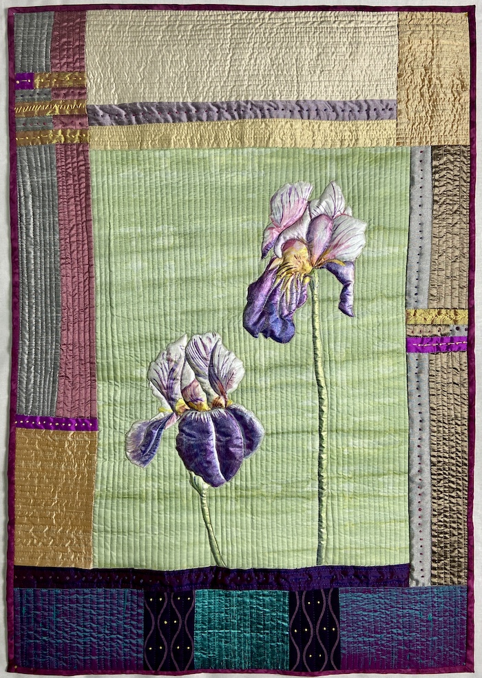Art quilt by Allison Wilbur of two iris on a green background surrounded by a pieced border. Flowers are painted on silk with straight line machine quilting in background.