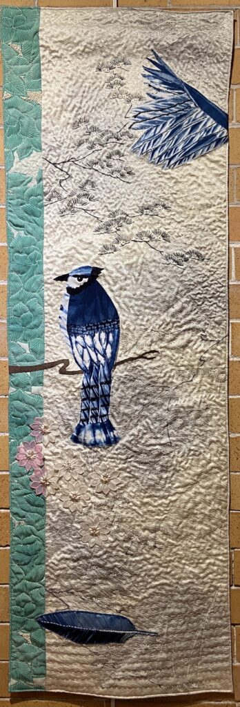 Spring Awakening art quilt by Allison Wilbur. Image of a blue jay sitting on a branch with a feather on the ground.