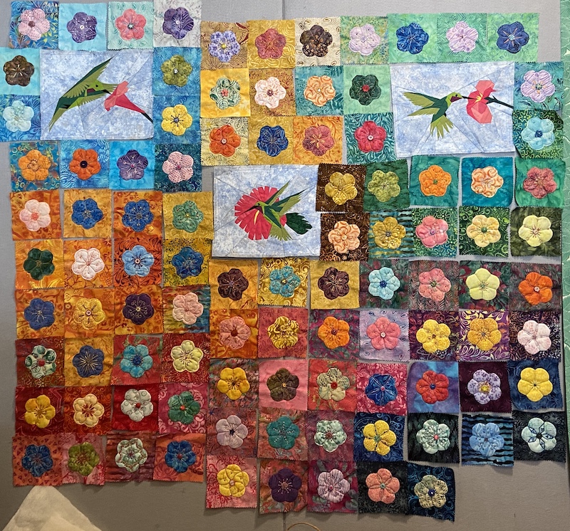 Appliquéd flowers and paper pieced hummingbird quilt blocks arranged on a design wall.