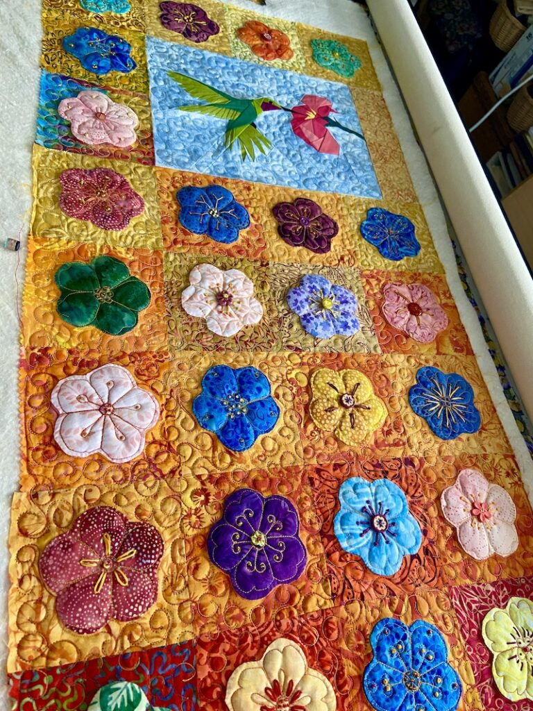 Quilt top with appliquéd flowers on the long arm quilting machine. Fine meandering stitches in the background help blend fabric colors together.
