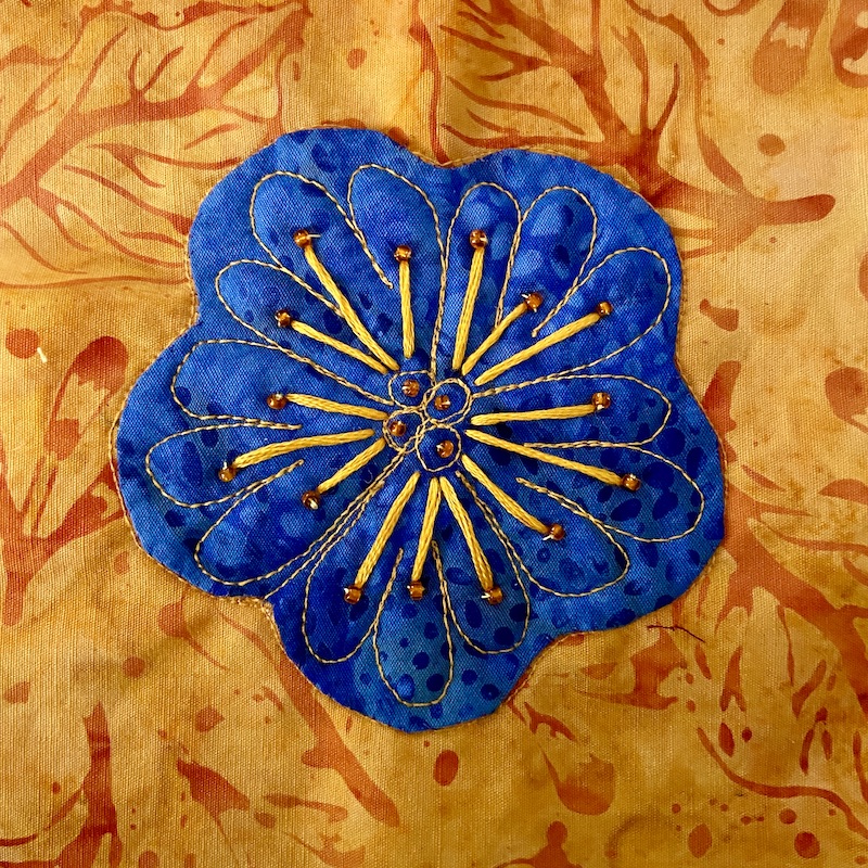 Blue flower with hand embroidery appliquéd onto an orange background with a button in the center.